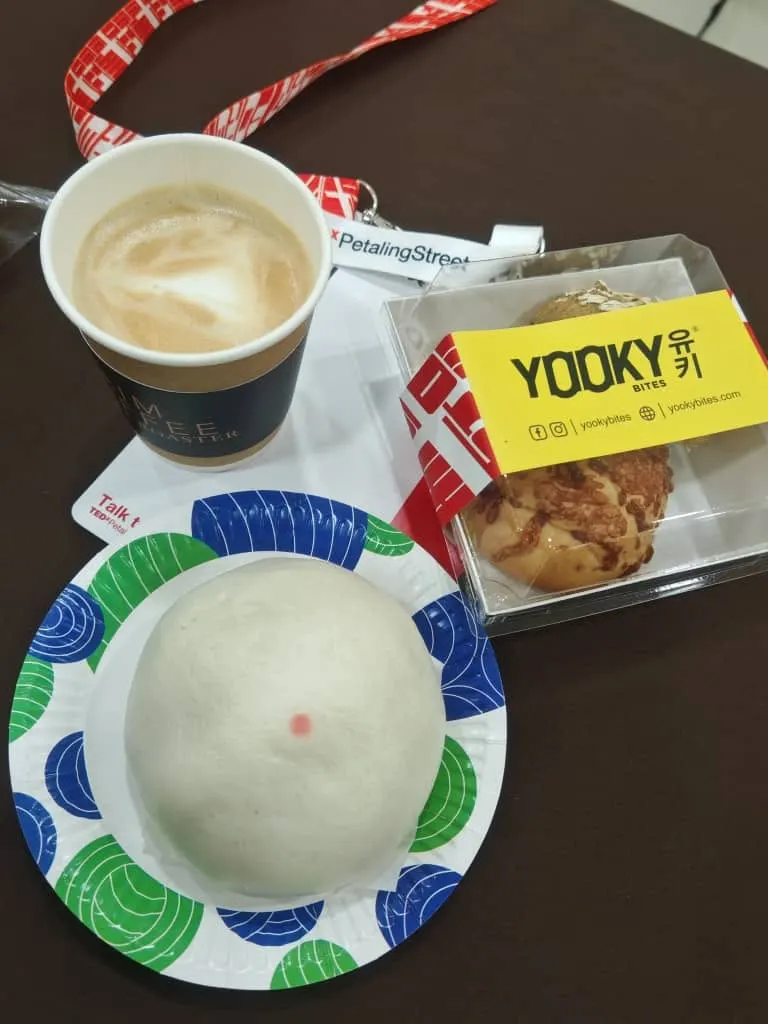 Coffee in a paper cup, a steamed bun on a paper plate and a boxed bun at TEDxPetalingStreet 2024