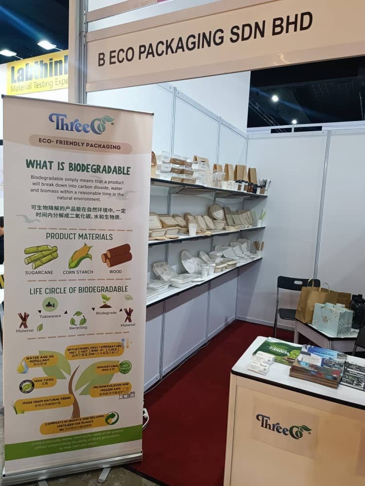 Sepanduk ThreeCo “Apa Itu Biodegradasi” di sebelah rak pameran pembungkusan eko di gerai B Eco Packaging